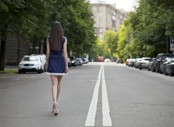 Young beautiful woman in a blue short dress walking on the road — Stock Photo, Image