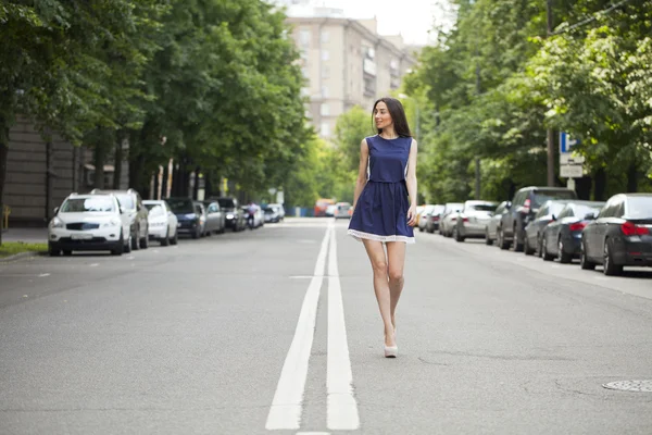 Young beautiful woman in a blue short dress walking on the road — Stock Photo, Image