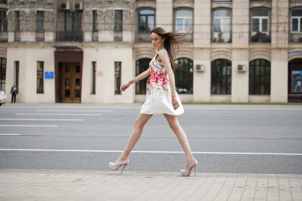 Jeune belle femme brune en robe de fleurs blanches marchant sur — Photo