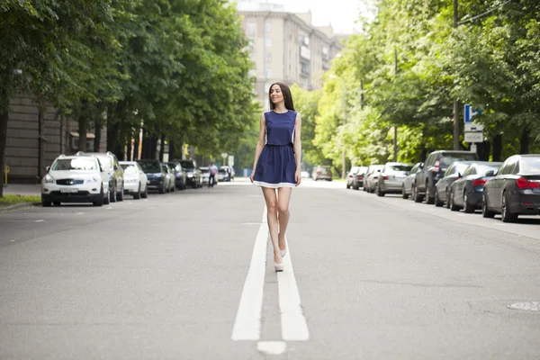 Jovem mulher bonita em um vestido curto azul andando na estrada — Fotografia de Stock