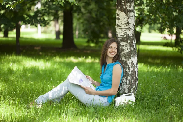 Happy woman leafing through a magazine while sitting in the summ — Stock Photo, Image