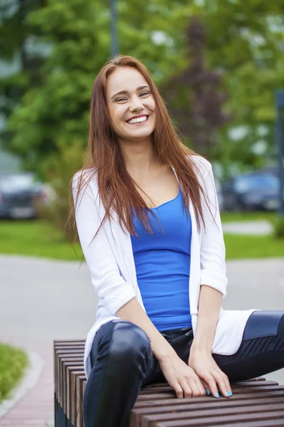 Jovem menina bonita sentada em um banco no parque de verão — Fotografia de Stock