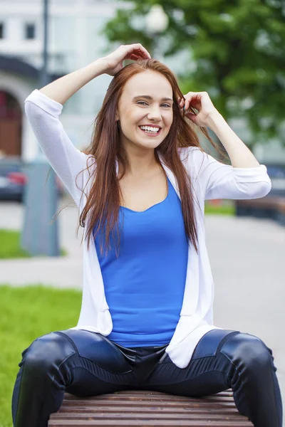 Jeune belle fille assise sur un banc dans le parc d'été — Photo