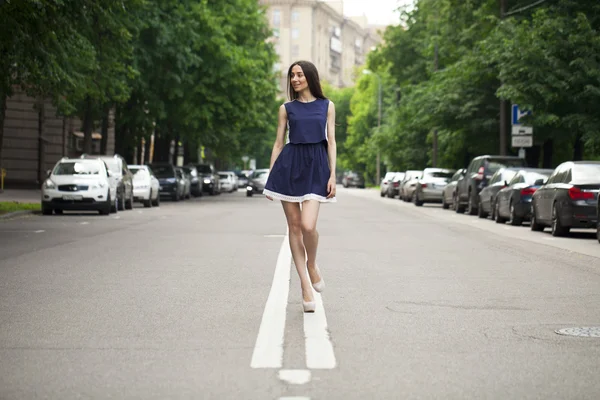 Young beautiful woman in a blue short dress walking on the road — Stock Photo, Image