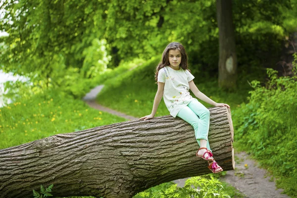 Little Girl in white dress sitting on tree trunk over green gras — Stock Photo, Image