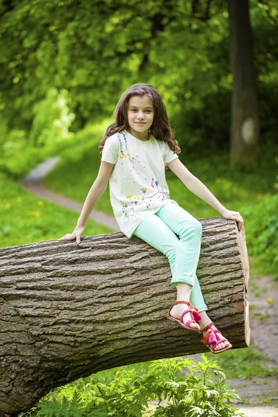 Little Girl in white dress sitting on tree trunk over green gras — Stock Photo, Image