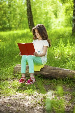 Orman ağaç kütüğü üzerinde oturup kitap ile sevimli küçük kız