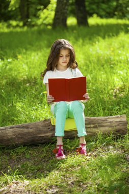 Orman ağaç kütüğü üzerinde oturup kitap ile sevimli küçük kız