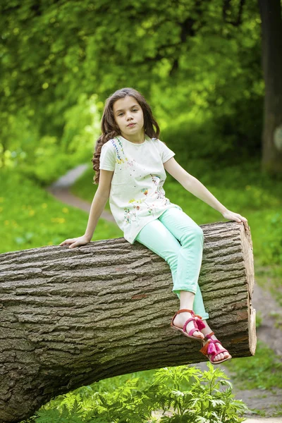 Petite fille en robe blanche assise sur un tronc d'arbre sur du gras vert — Photo