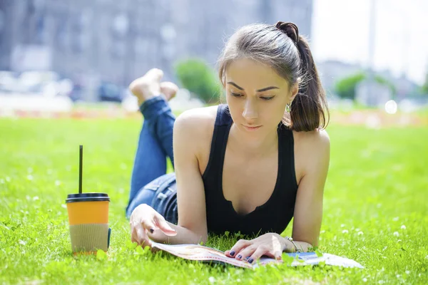 Junge Frau liest Zeitschrift liegend im Gras — Stockfoto