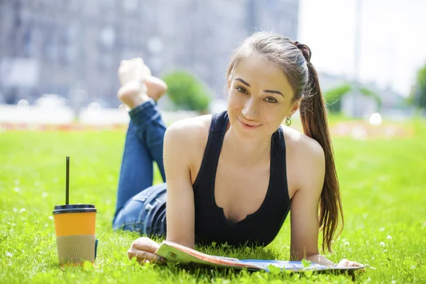 Ung kvinna läser tidningen liggande på gräs — Stockfoto