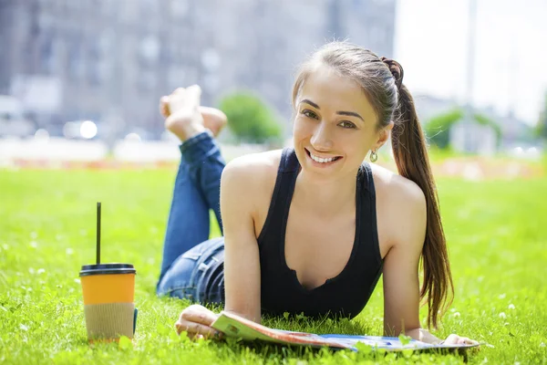 Giovane donna che legge rivista sdraiata sull'erba — Foto Stock