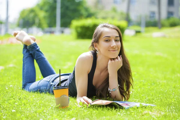 Ung kvinna läser tidningen liggande på gräs — Stockfoto
