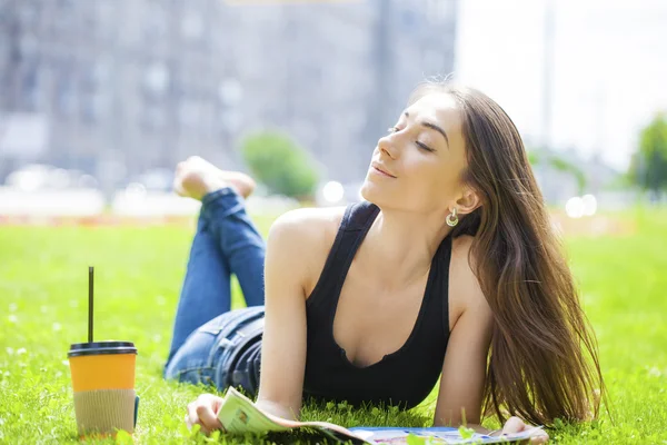 Giovane donna che legge rivista sdraiata sull'erba — Foto Stock