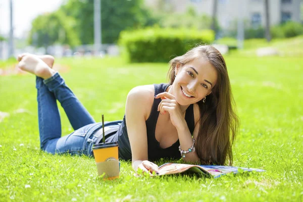 Junge Frau liest Zeitschrift liegend im Gras — Stockfoto