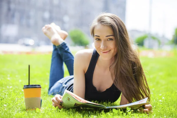 阅读杂志躺在草地上的年轻女子 — 图库照片