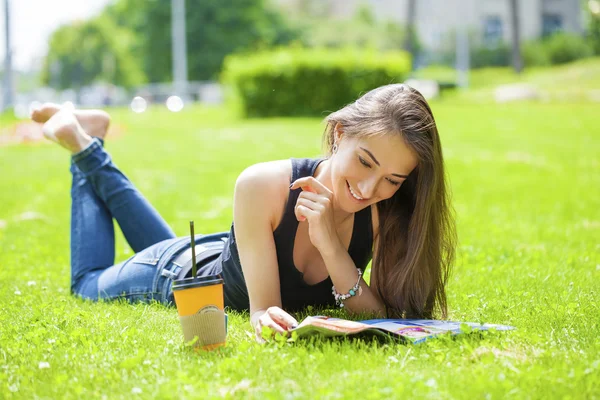 Jonge vrouw lezen tijdschrift liggen op gras — Stockfoto