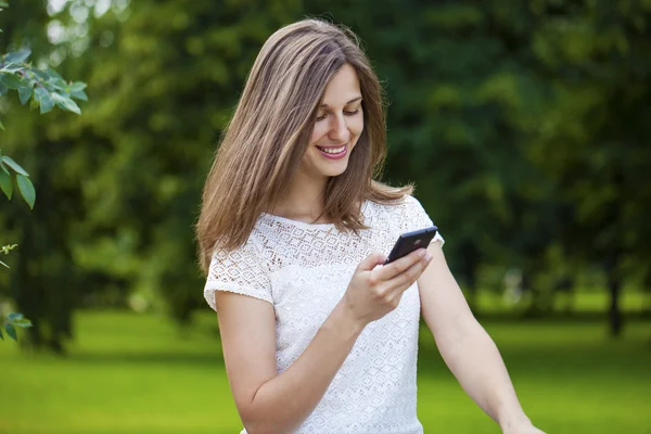 Mujer mensajes de texto en el teléfono inteligente caminando en el parque de verano — Foto de Stock