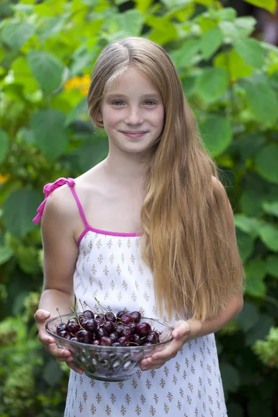 Beautiful girl holding a bowl of cherries in the garden — Stock Photo, Image