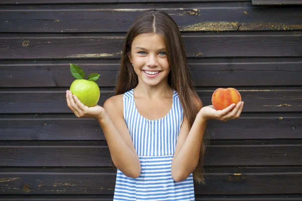 Little girl holding a green apple and a peach — Stock Photo, Image