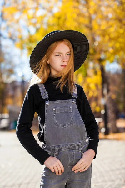 秋の公園を歩く黒い帽子の赤い髪の少女の肖像画 — ストック写真