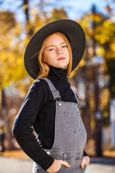 秋の公園を歩く黒い帽子の赤い髪の少女の肖像画 — ストック写真