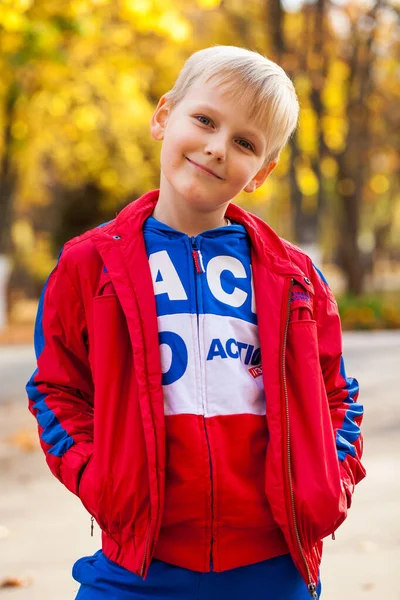 秋の公園を背景にした赤いトラックスーツの少年の肖像画 — ストック写真