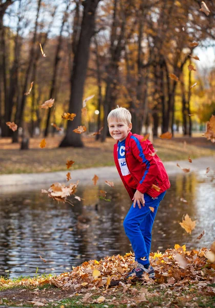 秋の公園を背景にした赤いトラックスーツの少年の肖像画 — ストック写真