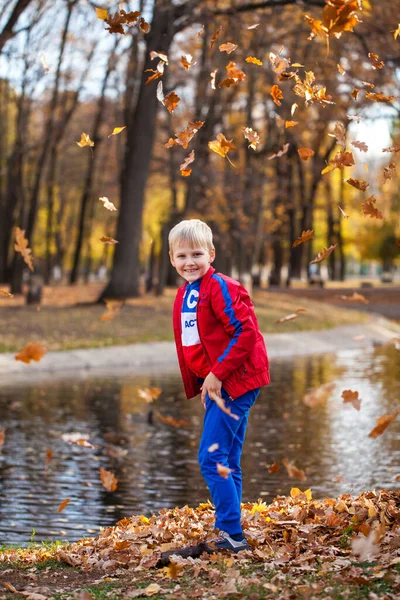 秋の公園を背景にした赤いトラックスーツの少年の肖像画 — ストック写真