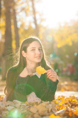 Mor kazaklı güzel bir kız düşen sonbahar yapraklarının üzerinde yatıyor.