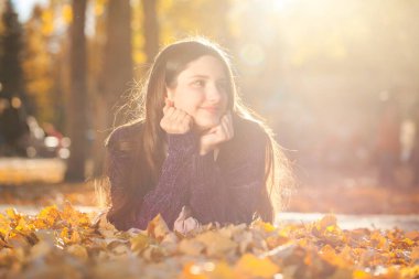 Mor kazaklı güzel bir kız düşen sonbahar yapraklarının üzerinde yatıyor.