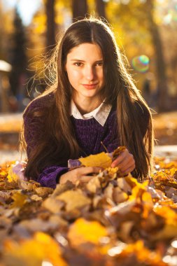 Mor kazaklı güzel bir kız düşen sonbahar yapraklarının üzerinde yatıyor.