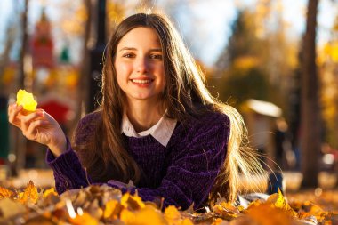 Mor kazaklı güzel bir kız düşen sonbahar yapraklarının üzerinde yatıyor.