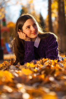 Mor kazaklı güzel bir kız düşen sonbahar yapraklarının üzerinde yatıyor.