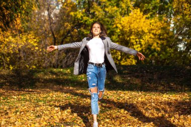 Güz parkında poz veren şık, yırtık pantolonlu güzel bir kızın tam boy portresi.