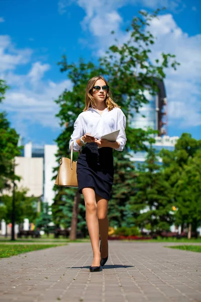 白地のブラウスと黒いスカートを着た若い実業家の肖像画が夏の公園を歩き — ストック写真
