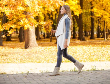 Güz yapraklarının etrafını saran güzel sarışın kızın açık hava moda fotoğrafı.