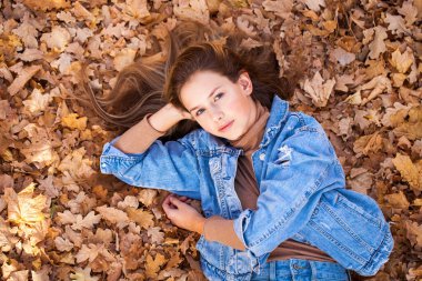 Üst manzara, sonbahar sarı yapraklarının arka planında güzel bir genç kızın portresi.