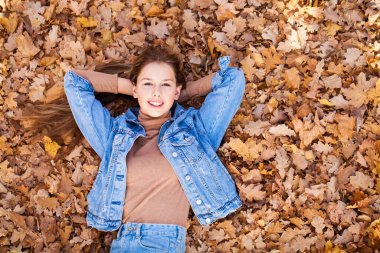 Üst manzara, sonbahar sarı yapraklarının arka planında güzel bir genç kızın portresi.