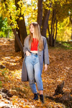 Gri ceketli, mavi kotlu, açık havada sonbahar parkında genç ve güzel bir kadının vücut portresi.
