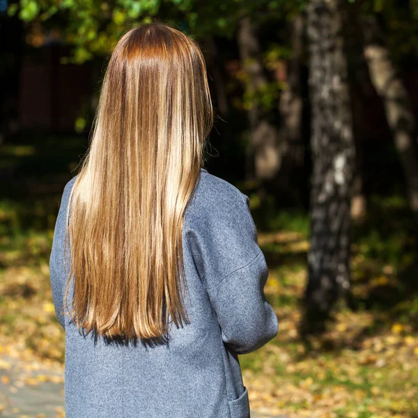 Blonde hair model. Back view girl in gray coat, autumn park outdoor