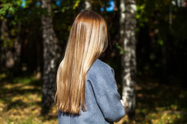 Blonde hair model. Back view girl in gray coat, autumn park outdoor