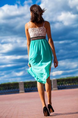 Tam boy portre. Turkuaz elbiseli genç ve güzel bir kız sette yürüyor.