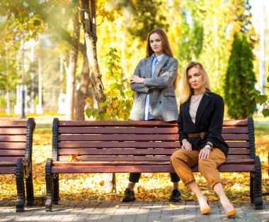 Orta yaşlı bir anne ve genç kızının sonbahar parkındaki portresi.