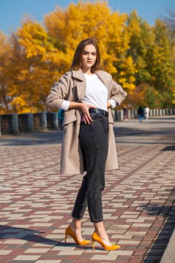 Bej ceketli ve siyah kotlu güzel bir esmer kızın vücut portresi.