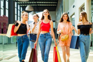 Genç mutlu kızlar alışveriş merkezinde yürüyor.
