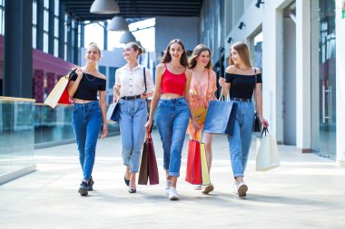 Genç mutlu kızlar alışveriş merkezinde yürüyor.