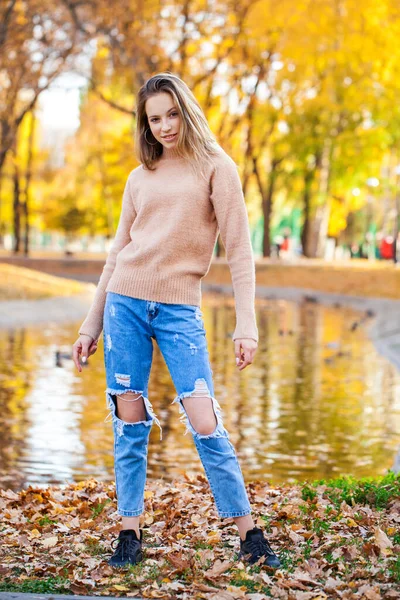 스웨터를 공원에서 포즈를 취하고 찢어진 청바지를 소녀의 — 스톡 사진