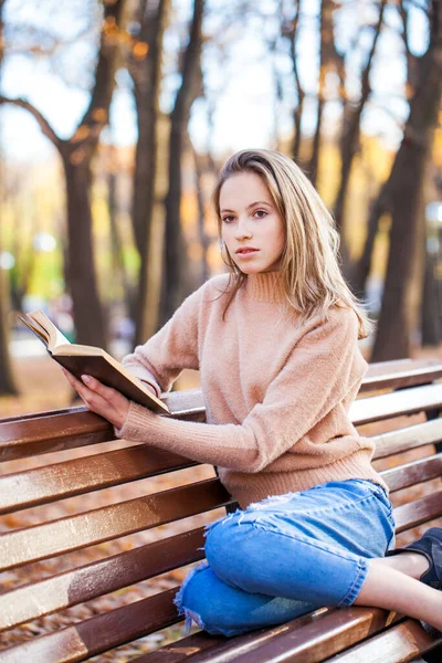 一个漂亮的小女孩带着一本书坐在秋天公园的长椅上 — 图库照片