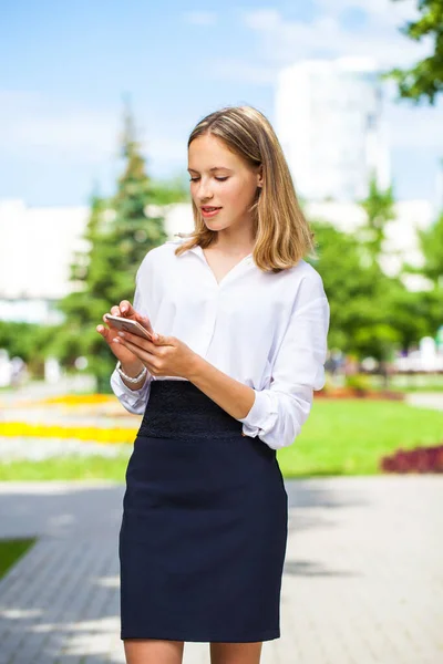 Portrait of a young assistant in a white blouse and with a phone in her hands posing outdoors
